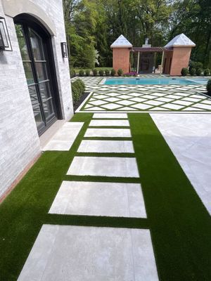 A paved stone walkway leads past a white brick building toward a rectangular swimming pool surrounded by geometric pavers.