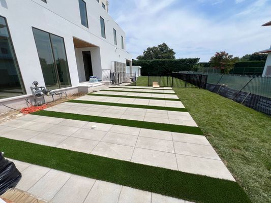 A modern white house patio with light-colored pavers separated by rows of artificial turf grass.
