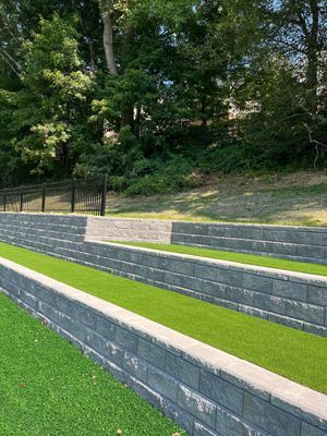 Three tiered retaining walls made of grey stone blocks with strips of artificial grass between them.