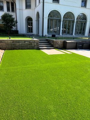 A lush green lawn leading to stone steps and a white multi-story building with large arched glass doors.