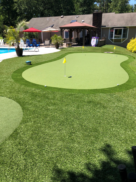 Backyard putting green with artificial turf, two yellow flags, a swimming pool, and a patio cover.