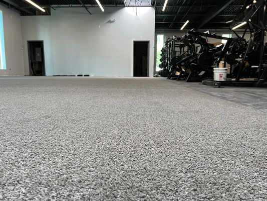 A light gray, speckled epoxy floor in a gym, with exercise equipment in the background.