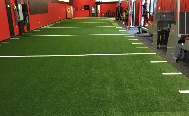 An indoor training facility featuring a green turf floor marked with white yard lines like an American football field.