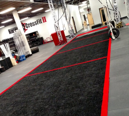 An indoor gym featuring a long black turf track with red borders and markings, set in a CrossFit facility.