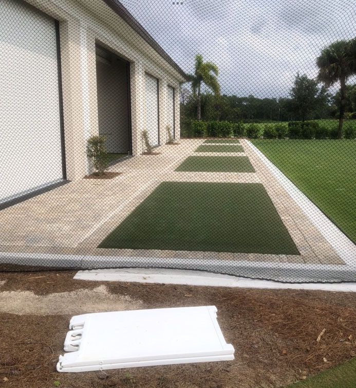 A paved patio with rectangular artificial turf inserts alongside a building, with a white vent cover in the foreground.