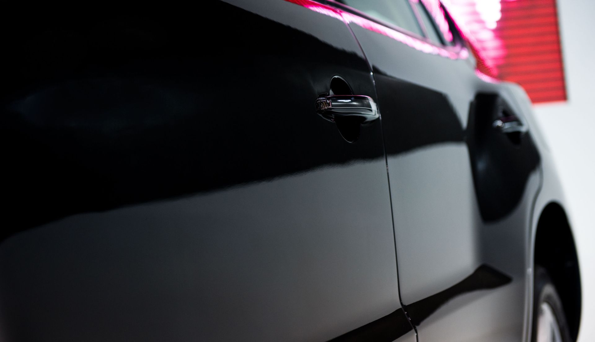 Close-up of a black car door with a silver handle against a red background