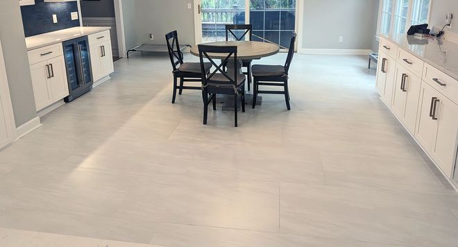 Bright, open kitchen with white cabinets, light wood-look floor, round table with chairs.