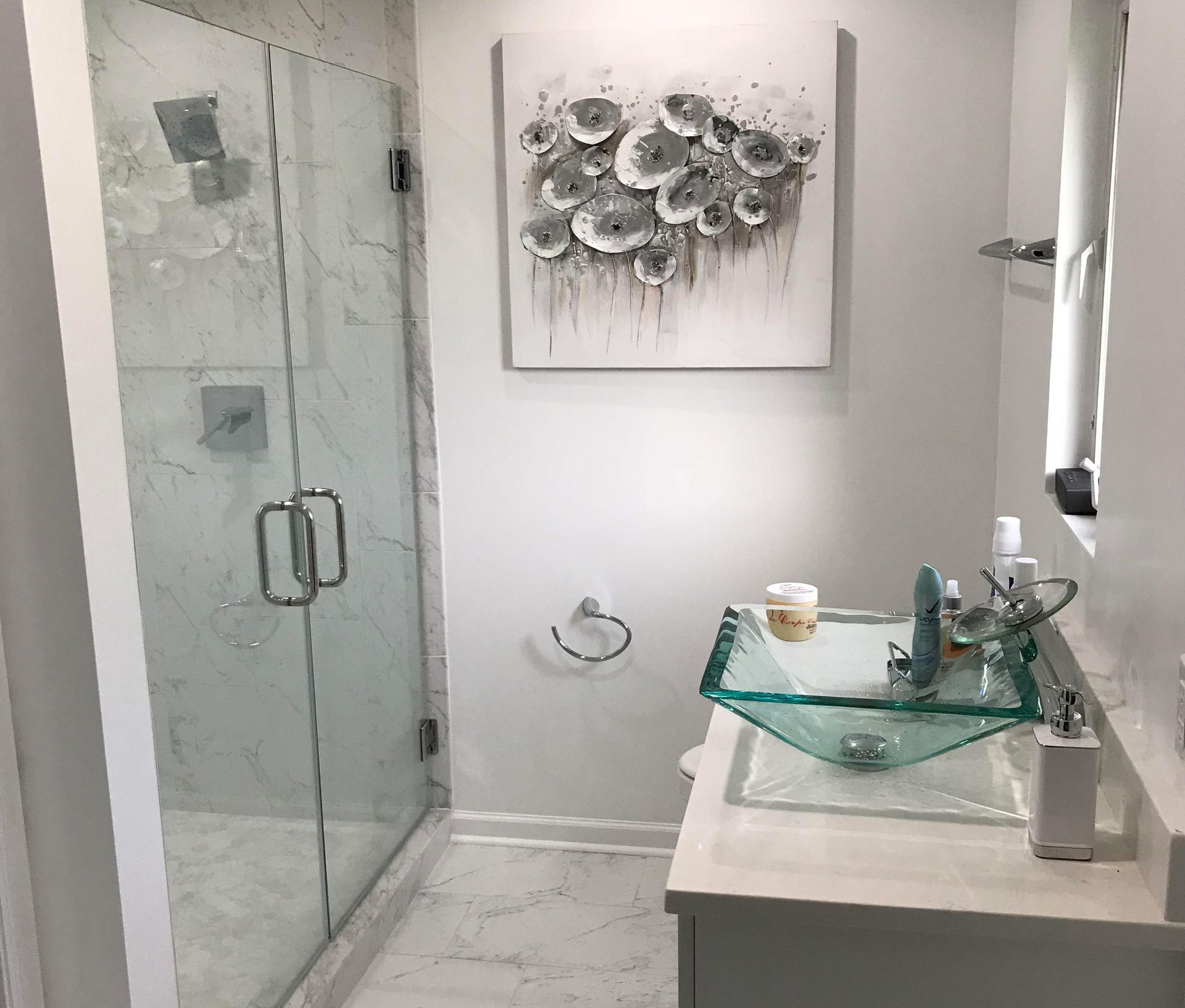 Bathroom with glass shower, modern glass sink, artwork of gray flowers, and white countertop.