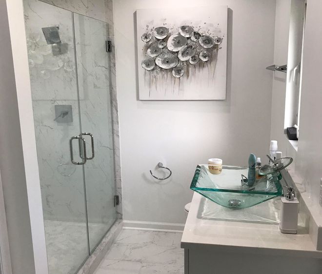 Bathroom with glass shower, modern glass sink, artwork of gray flowers, and white countertop.