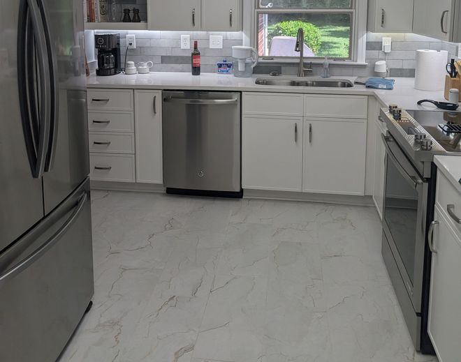 A modern kitchen with white cabinets, stainless steel appliances, and marble-look flooring.