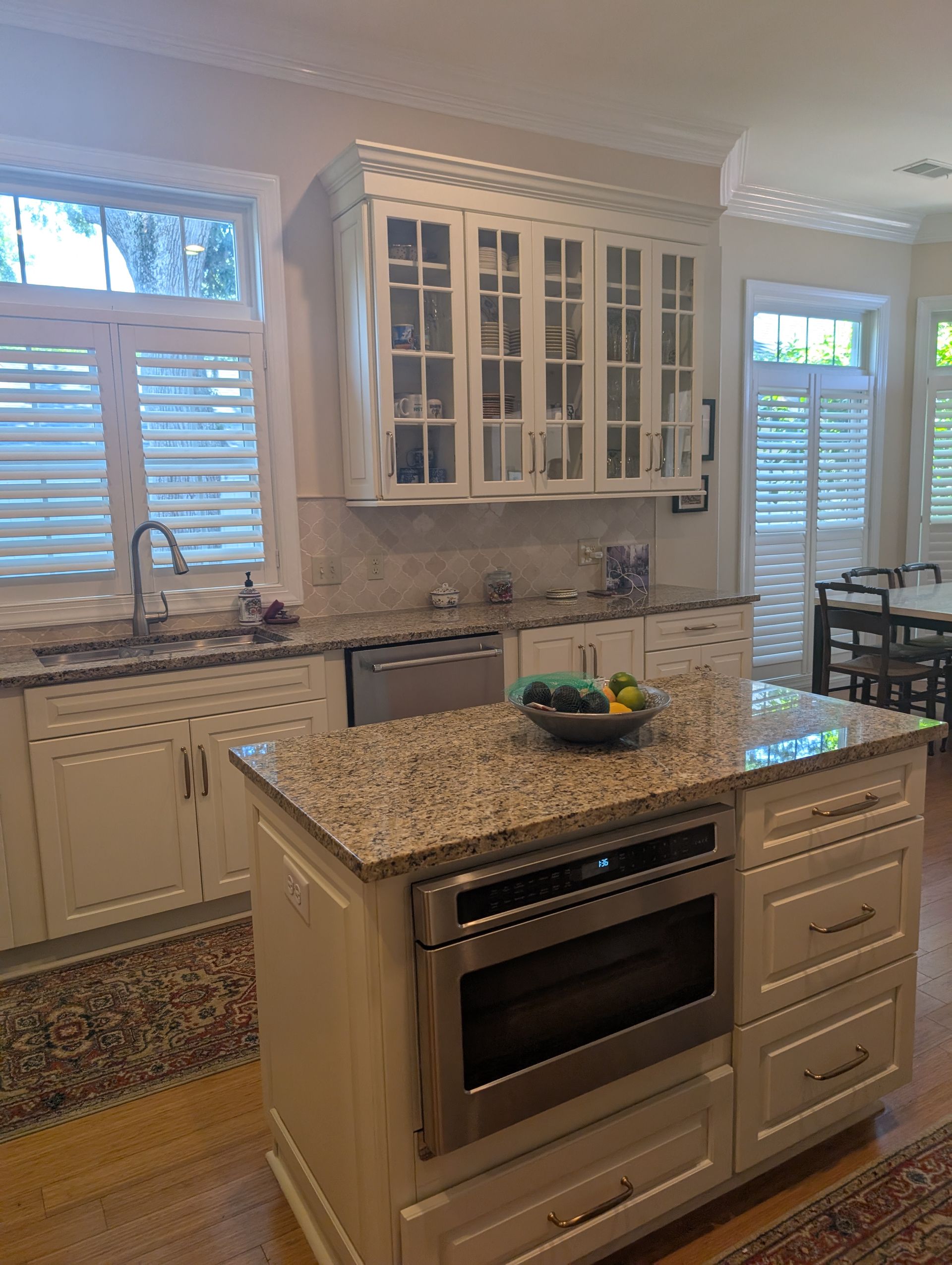 Kitchen with white cabinets, granite countertops, and an island with a built-in microwave and stainless steel appliances.