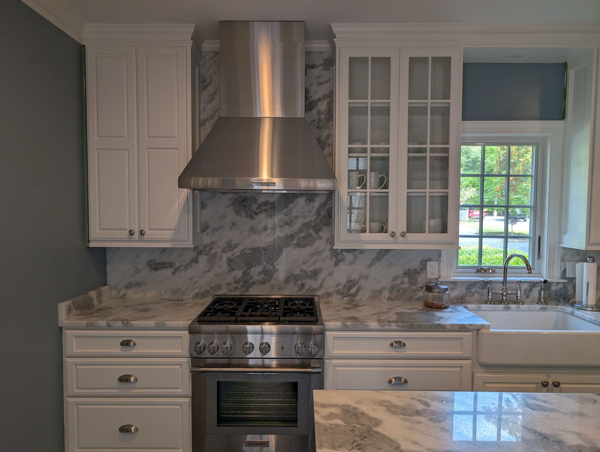 White kitchen with marble countertops, stainless steel appliances, and a window.