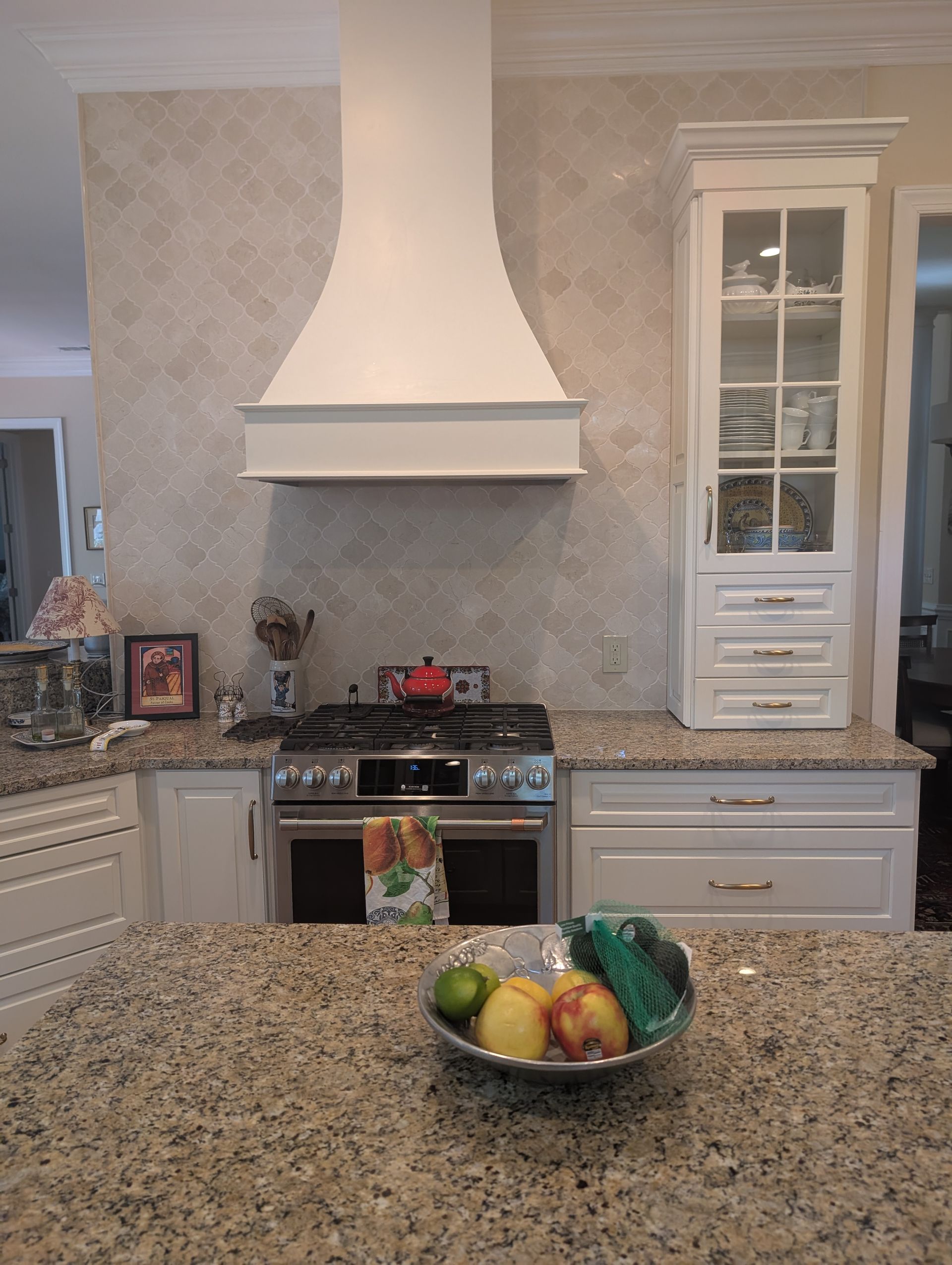 Kitchen with a white range hood, stove, and a cabinet. Granite countertops and a bowl of fruit.