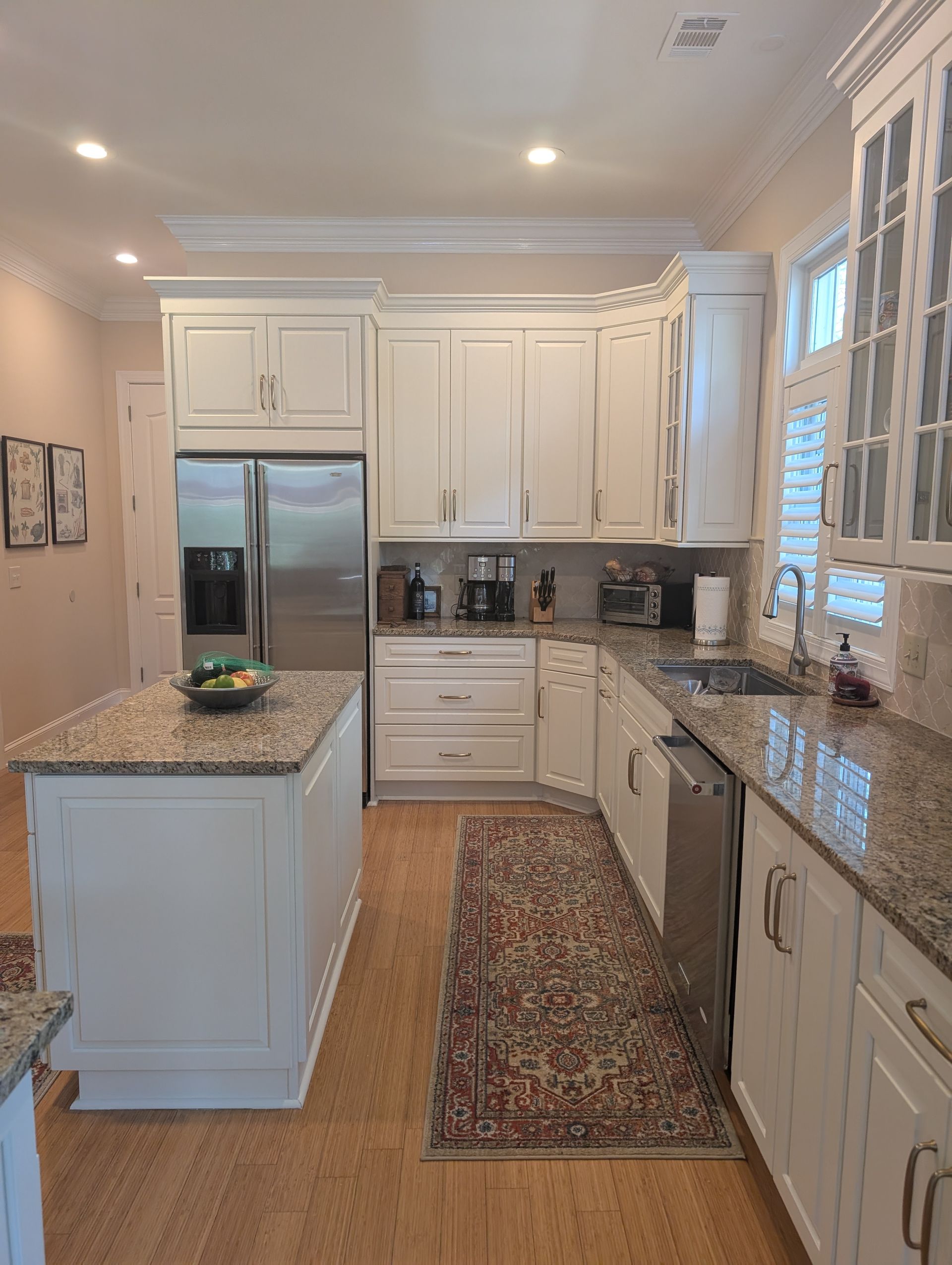White kitchen with island and appliances; wood floor and patterned rug.
