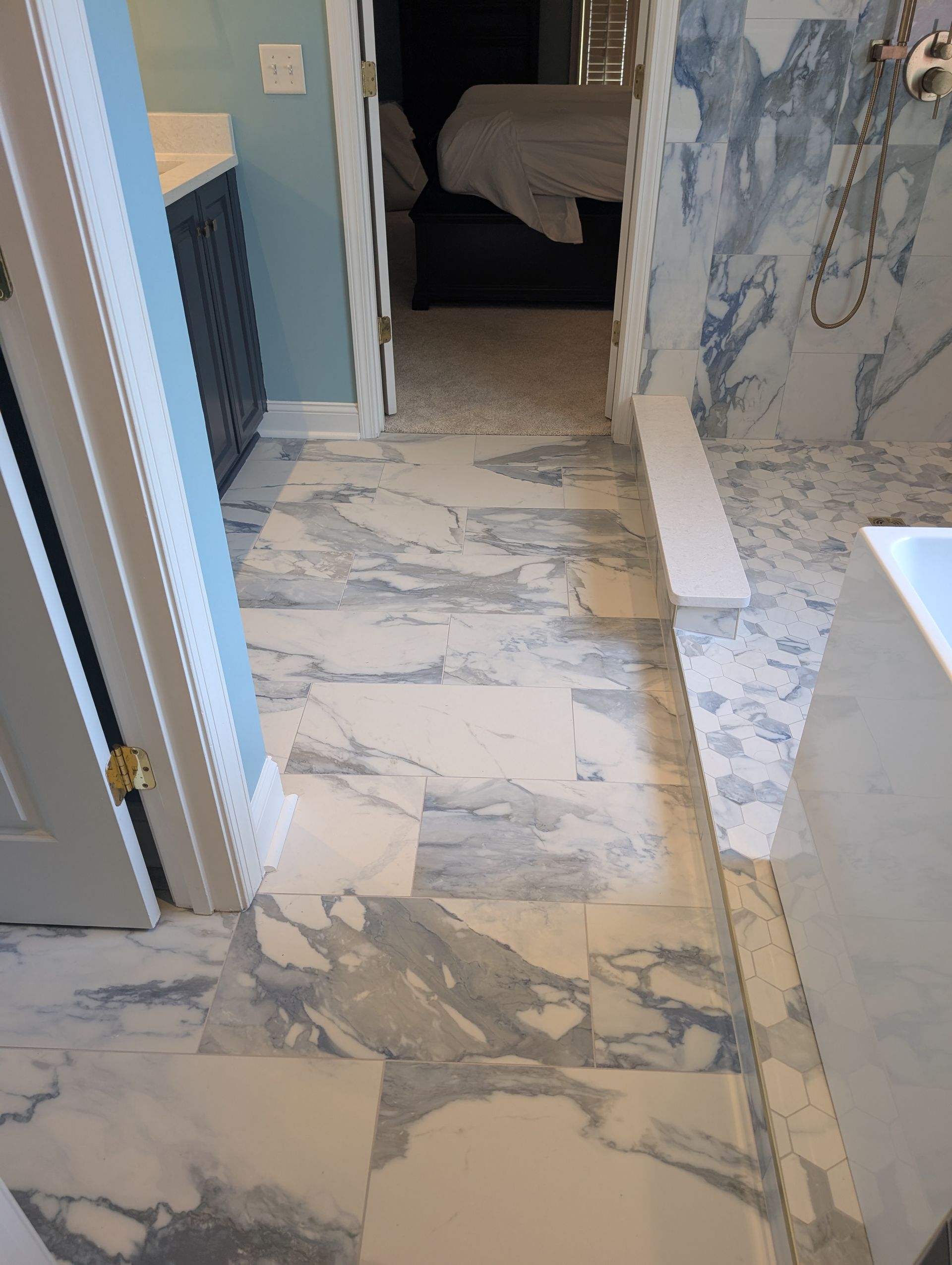 Bathroom with marble-patterned tile floor, blue and white walls, and a view into a bedroom.