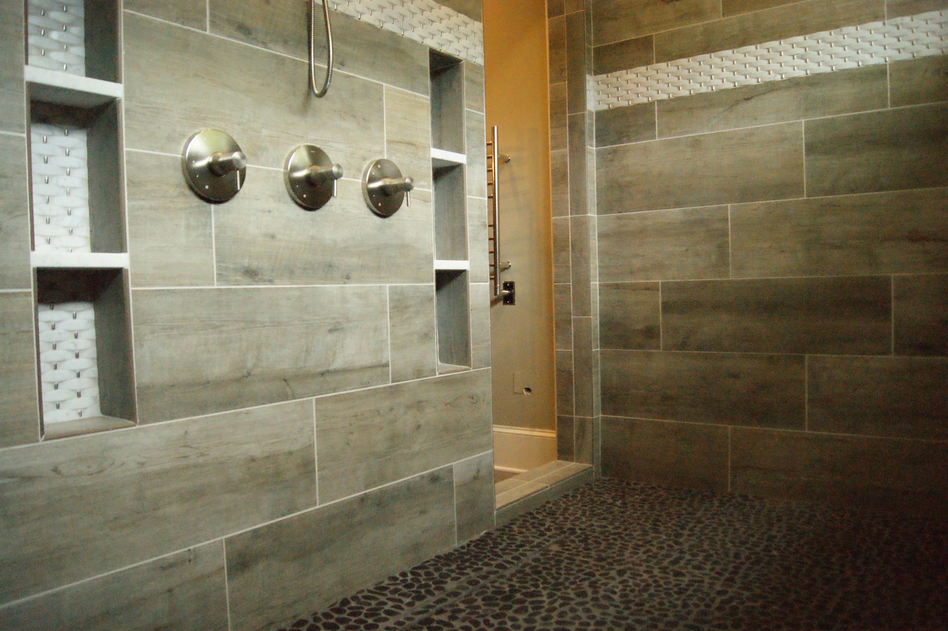 Bathroom with grey tile walls, showerhead, built-in shelves, and pebble floor.