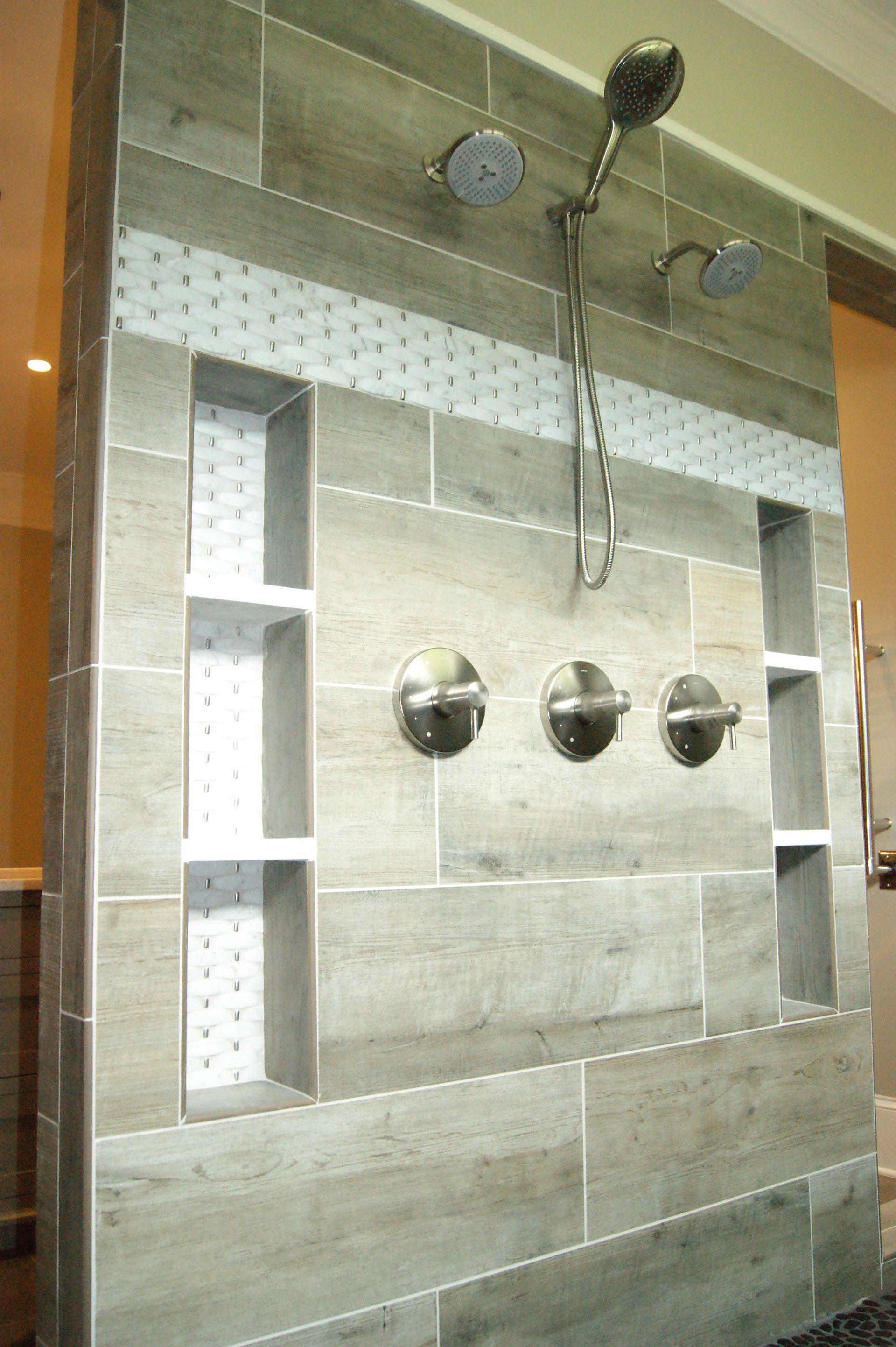 Shower wall with wood-look tile, three built-in shelves, and three showerheads. Stainless steel fixtures.