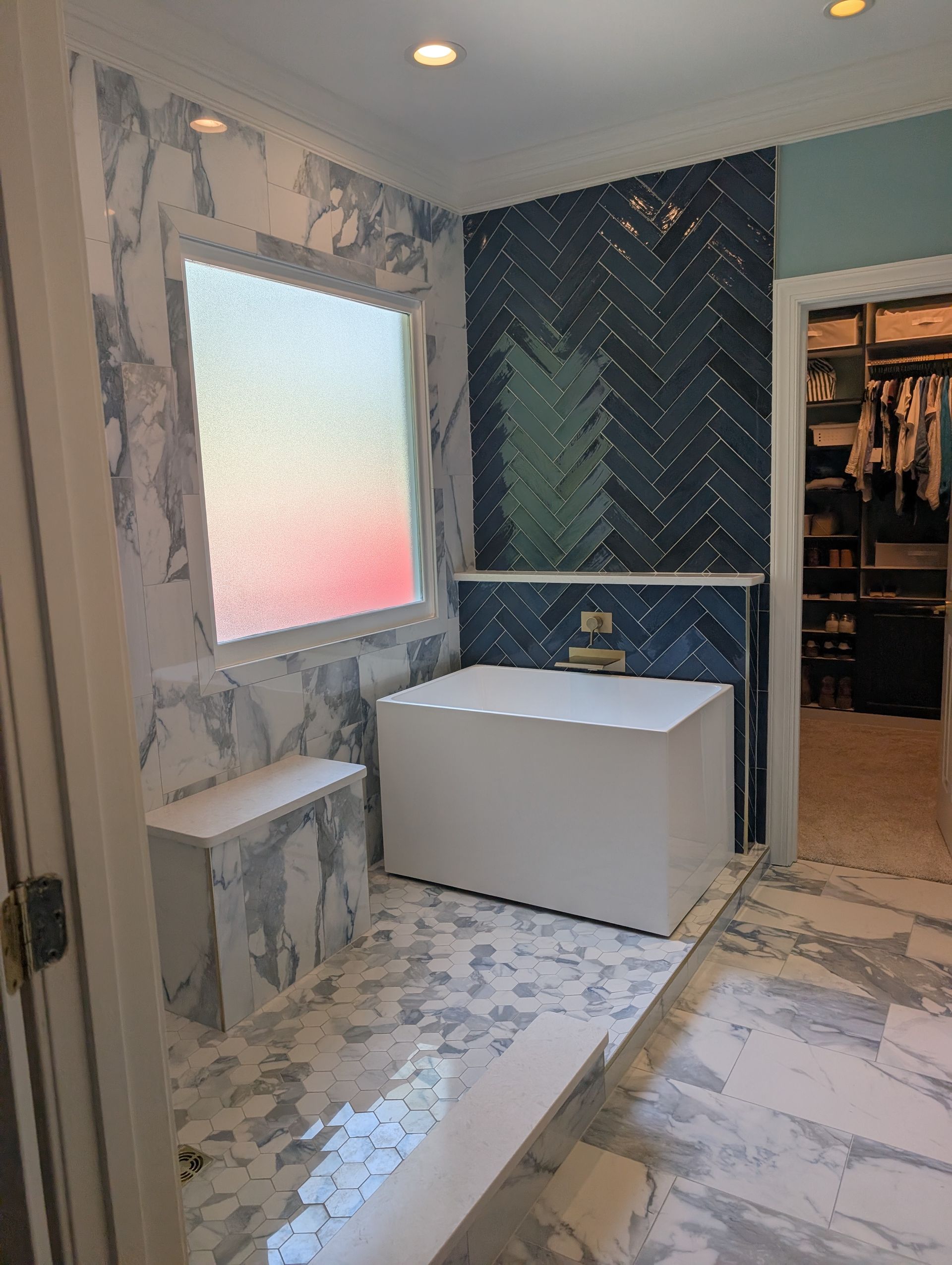 Modern bathroom with blue and white marble tiling, white tub, and walk-in closet in the background.