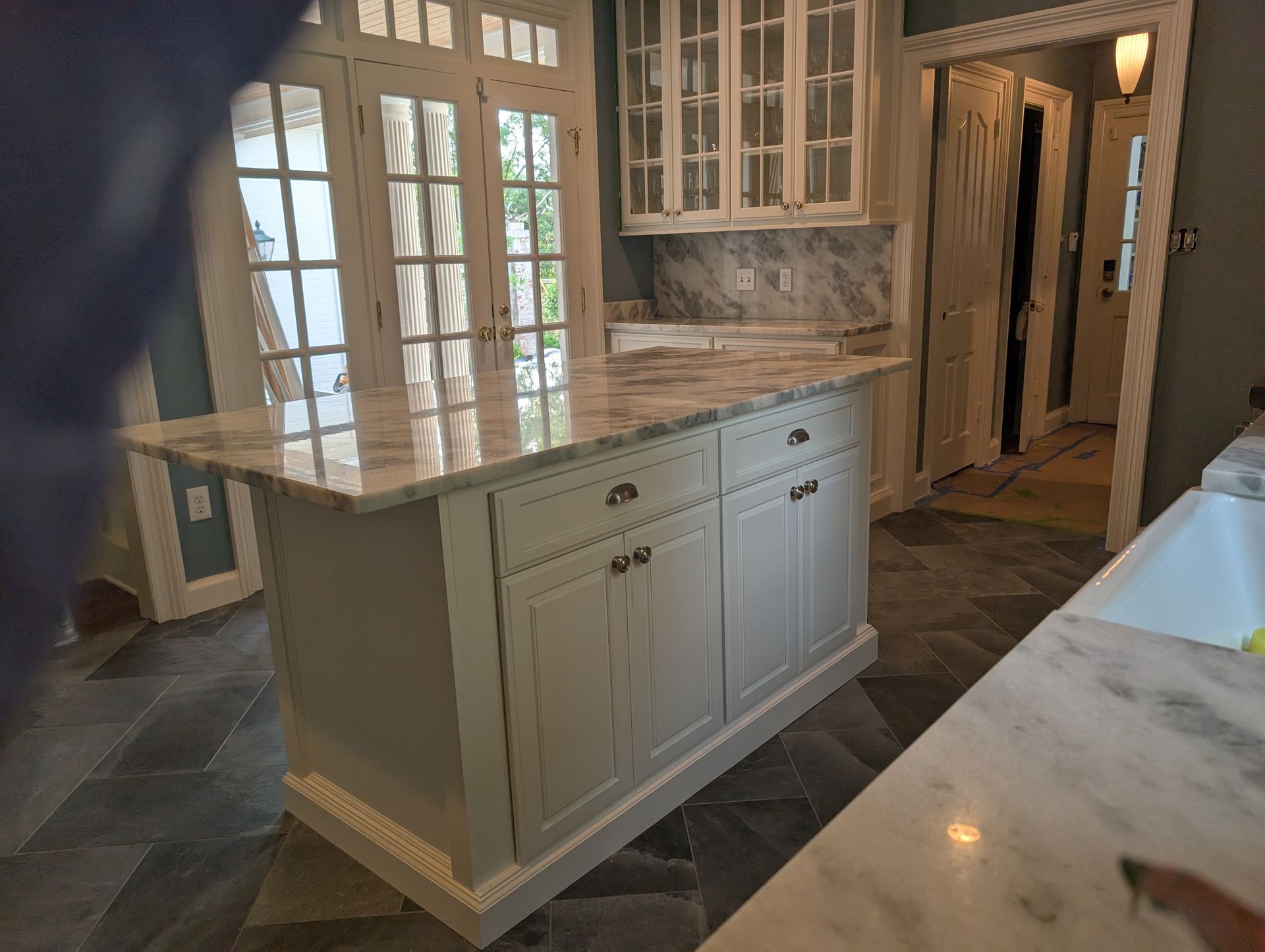 Kitchen with white cabinets, marble countertop, French doors, and stone floor.