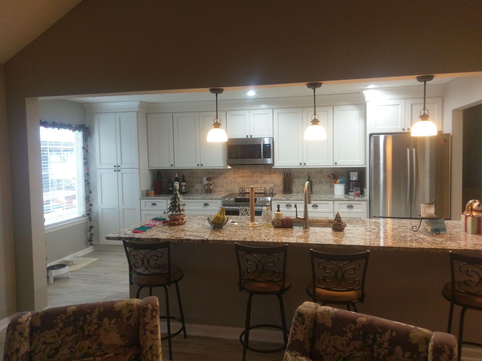 Bright kitchen with white cabinets, granite countertop island, stainless steel appliances, and pendant lights.
