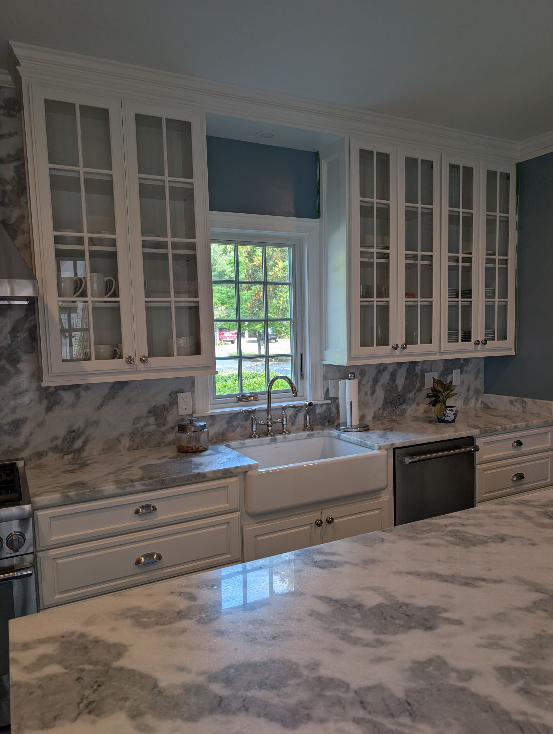 White kitchen with marble countertops, cabinets, and a farmhouse sink under a window.