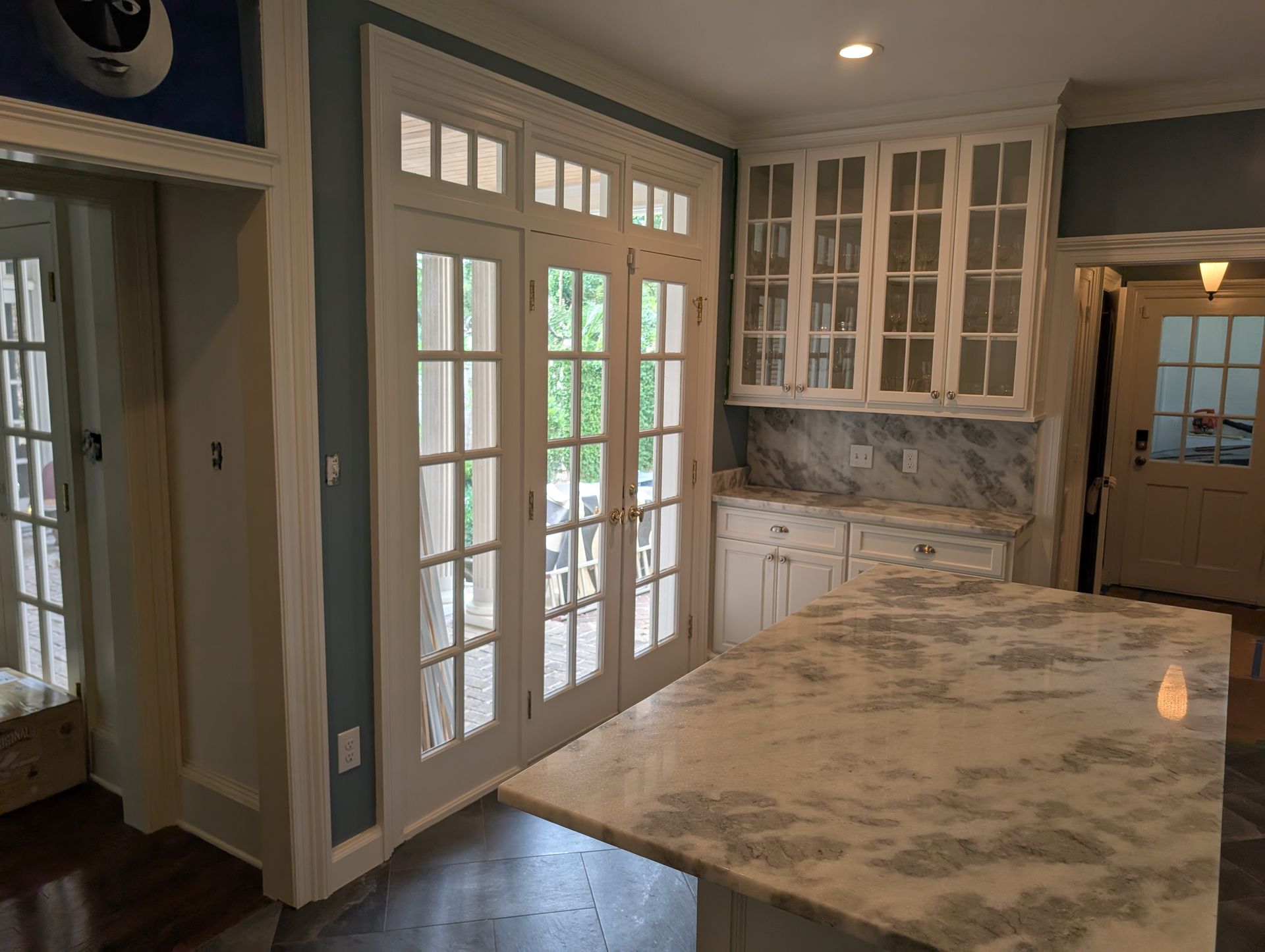 Kitchen with French doors, island with marble countertop, white cabinets, and a hallway.