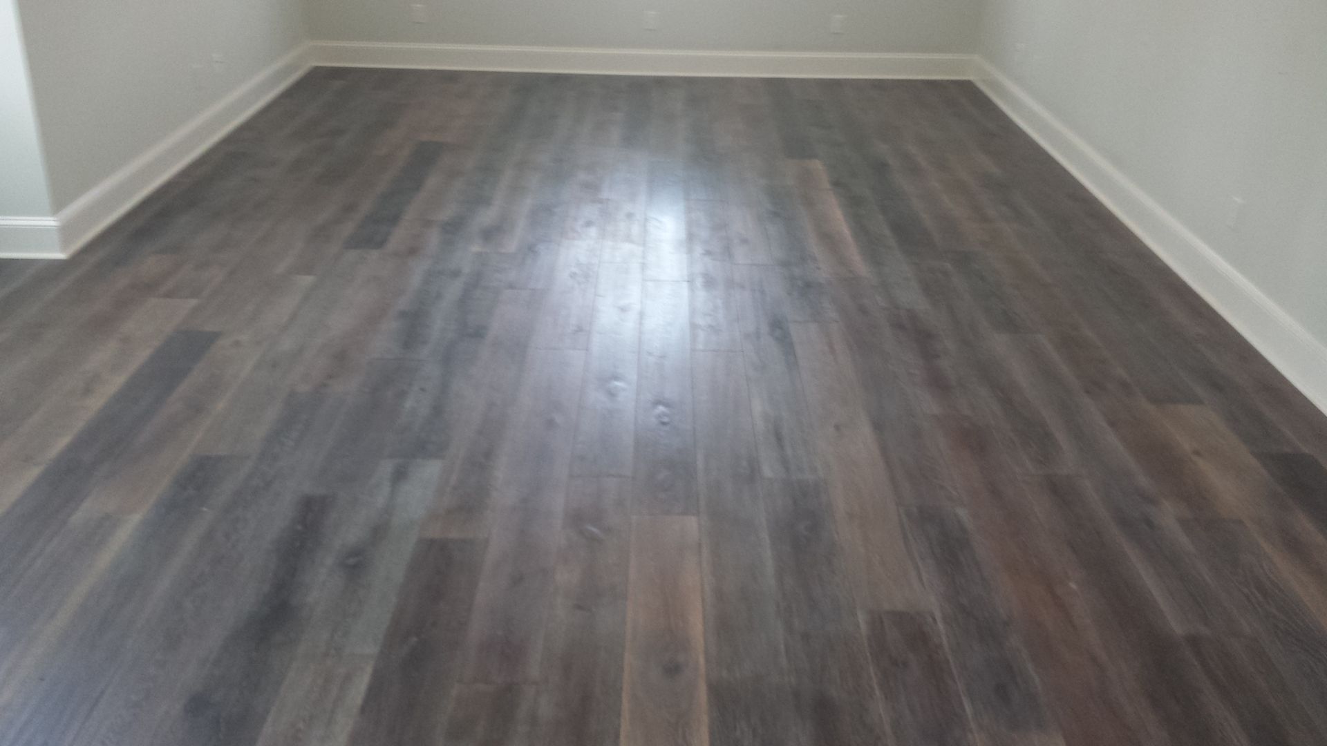 Dark brown wood-look flooring in a room with white baseboards and walls.