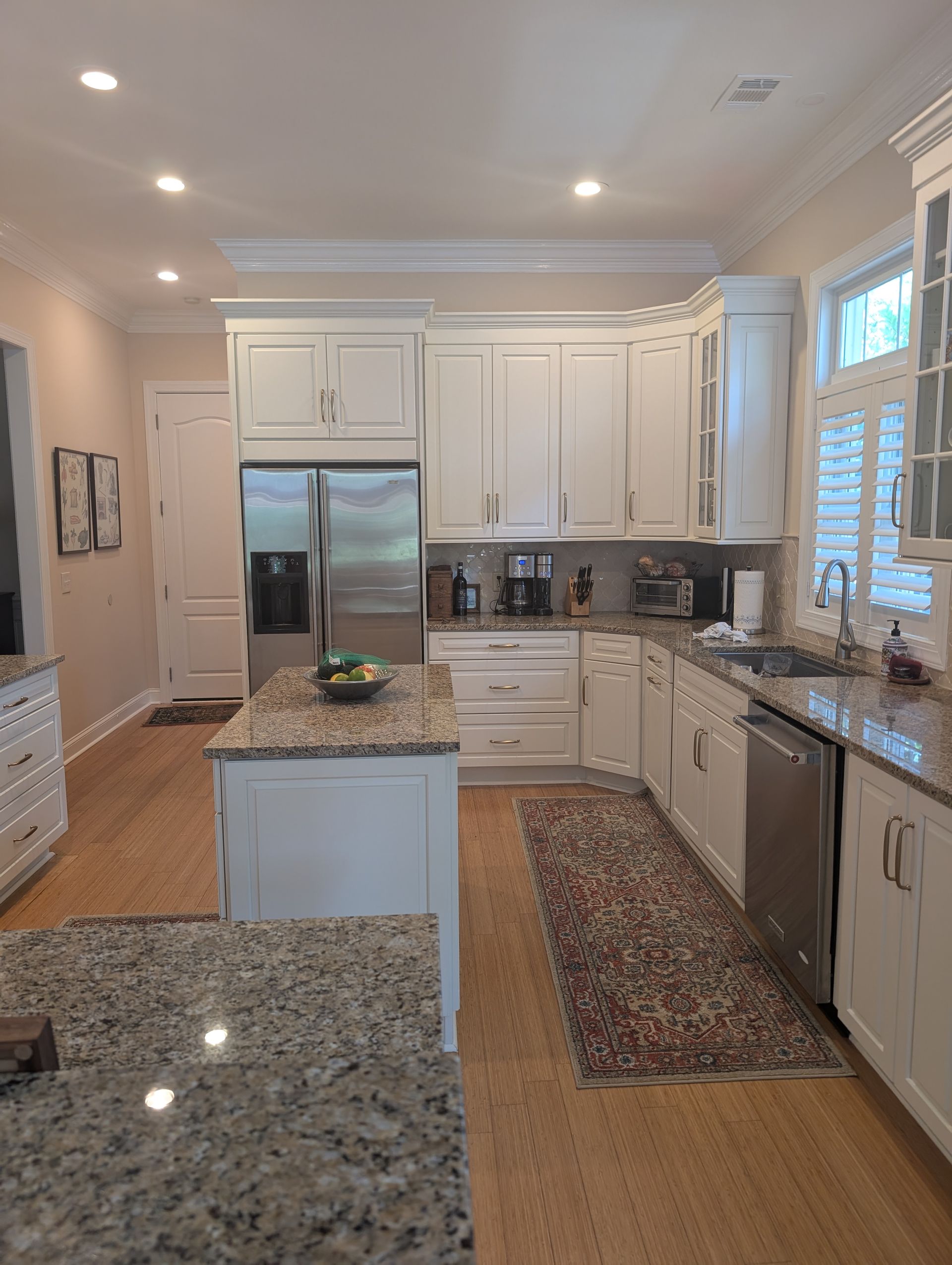 White kitchen with island, stainless steel appliances, granite countertops, and wood flooring.