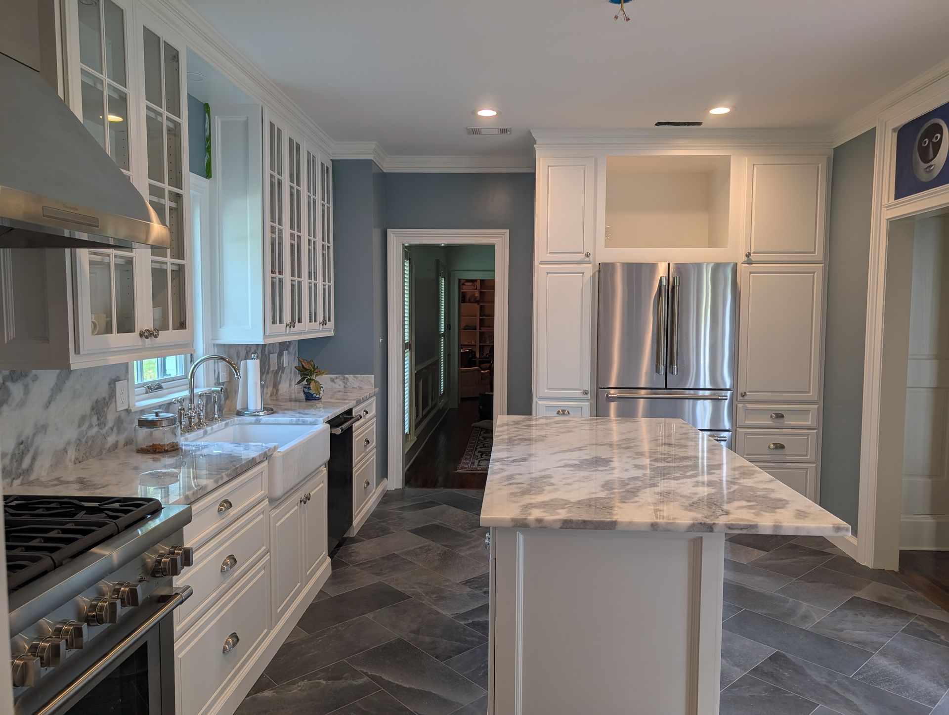 Elegant white kitchen with marble countertops, stainless steel appliances, and gray herringbone floor.