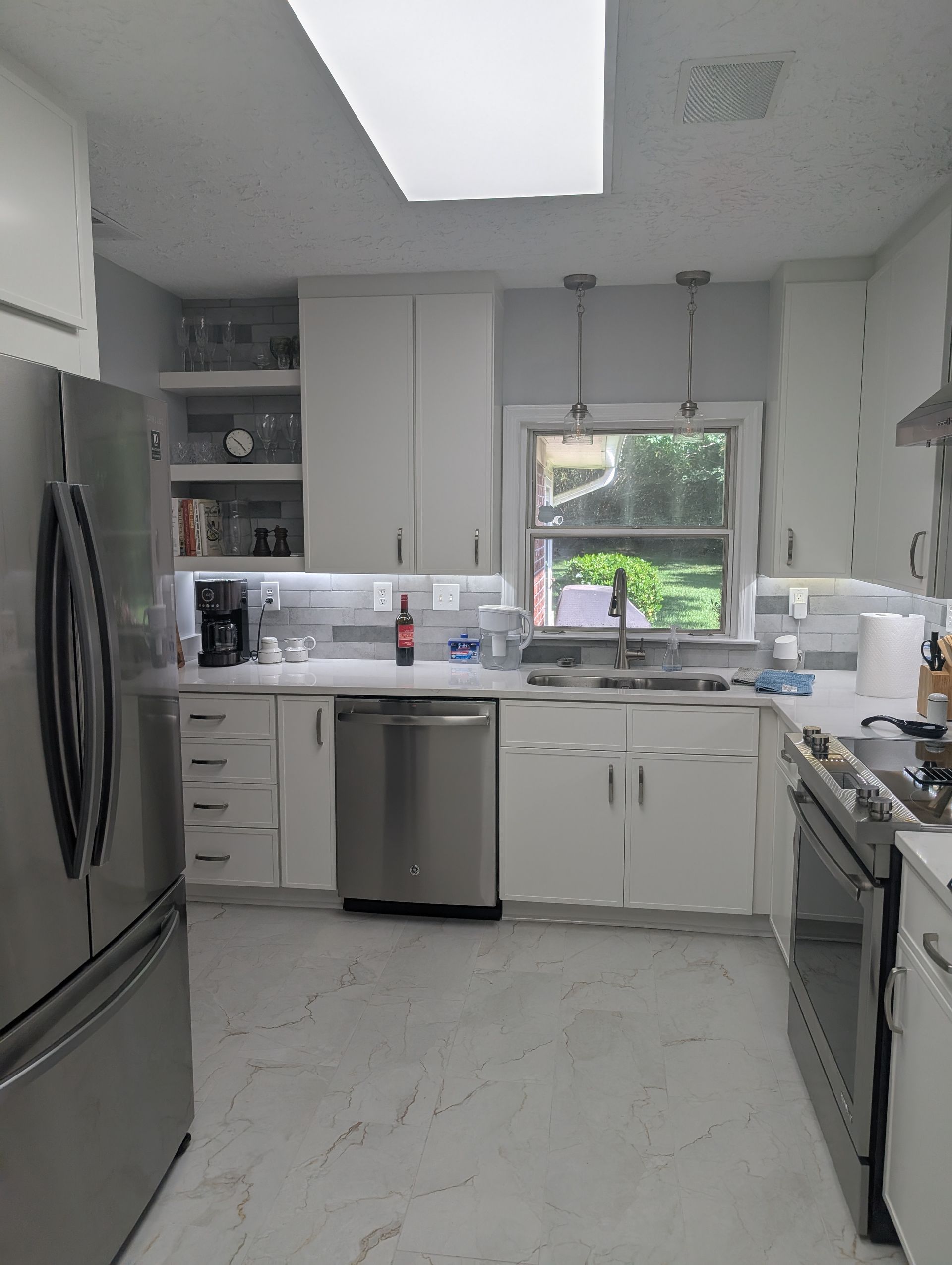 White kitchen with stainless steel appliances, cabinets, and a window.