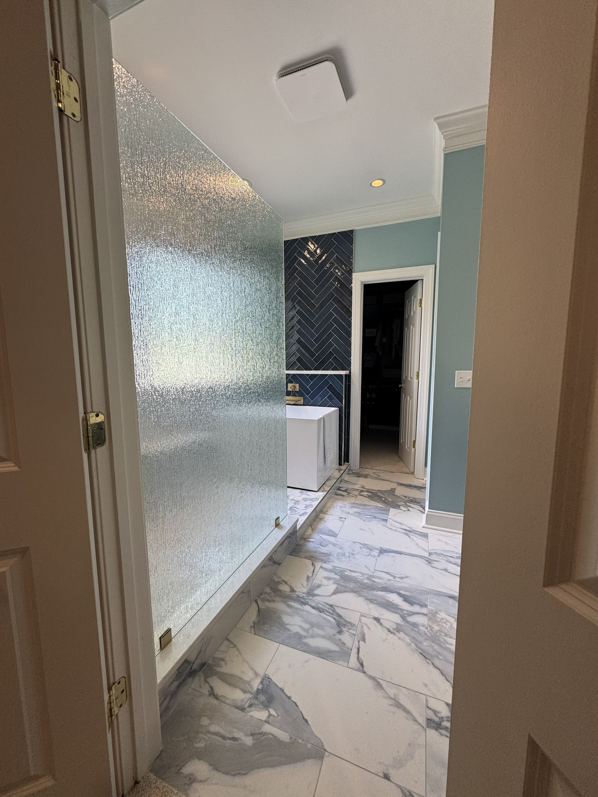 Bathroom with textured glass shower, marble flooring, and light blue walls.