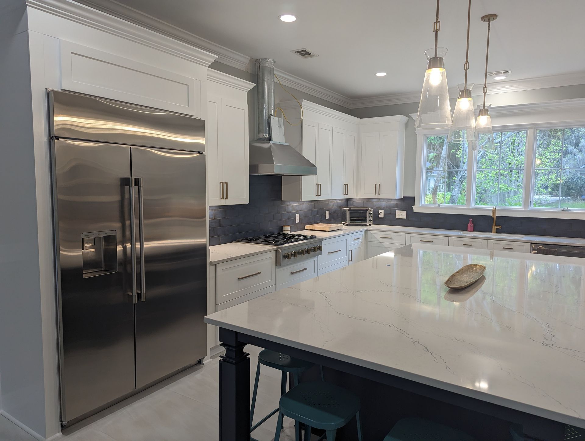 Modern kitchen with stainless steel refrigerator, white cabinets, island, and pendant lights.