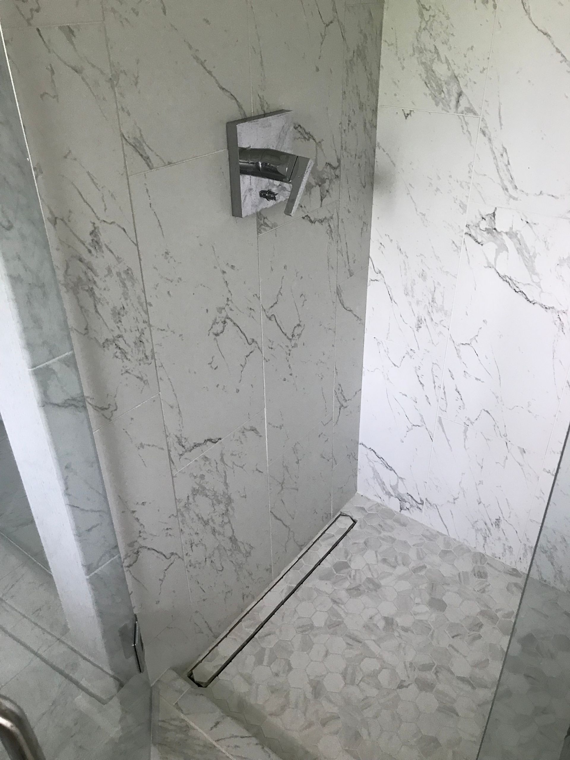 Shower with white marble walls, chrome fixtures, and a linear drain.