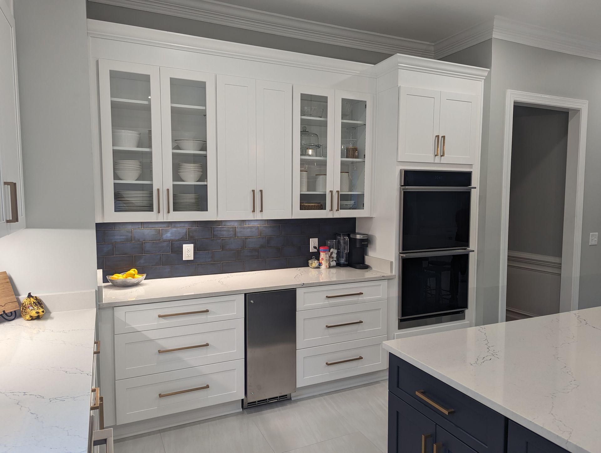 White kitchen cabinets with glass doors, a built-in oven, and a blue tile backsplash.