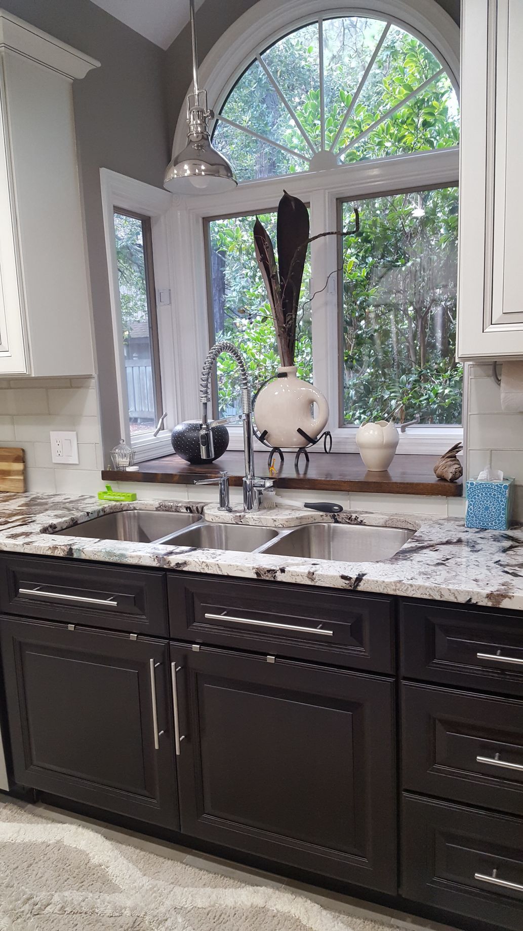 Kitchen sink with dark cabinets, granite countertops, and large window with outside view.