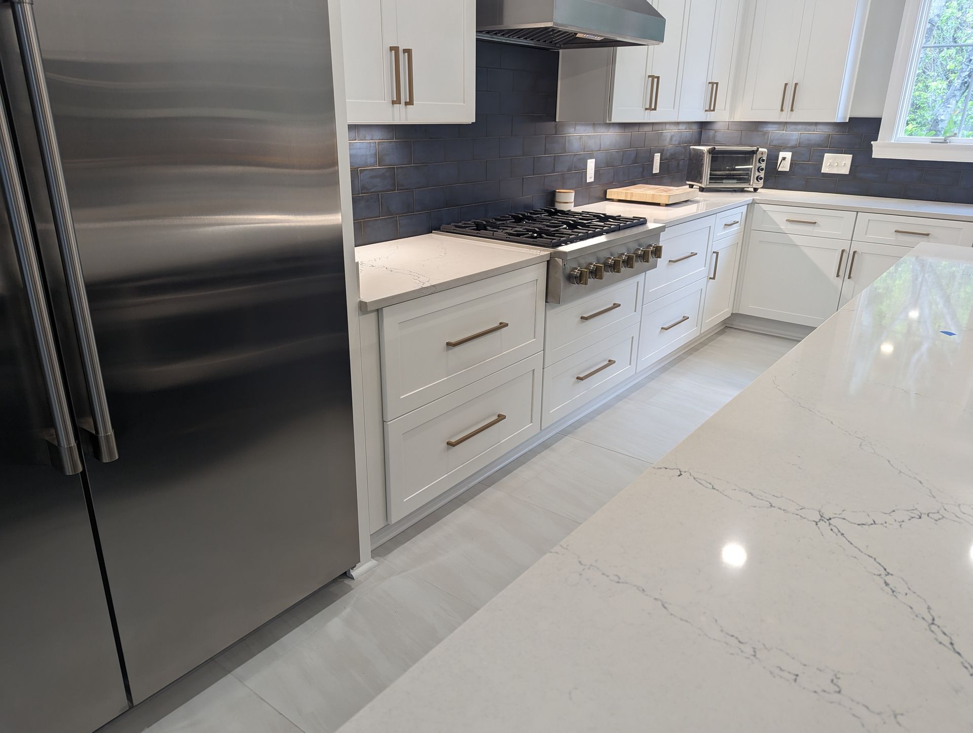Modern kitchen with white cabinets, stainless steel appliances, and a gas range. White countertops and island.