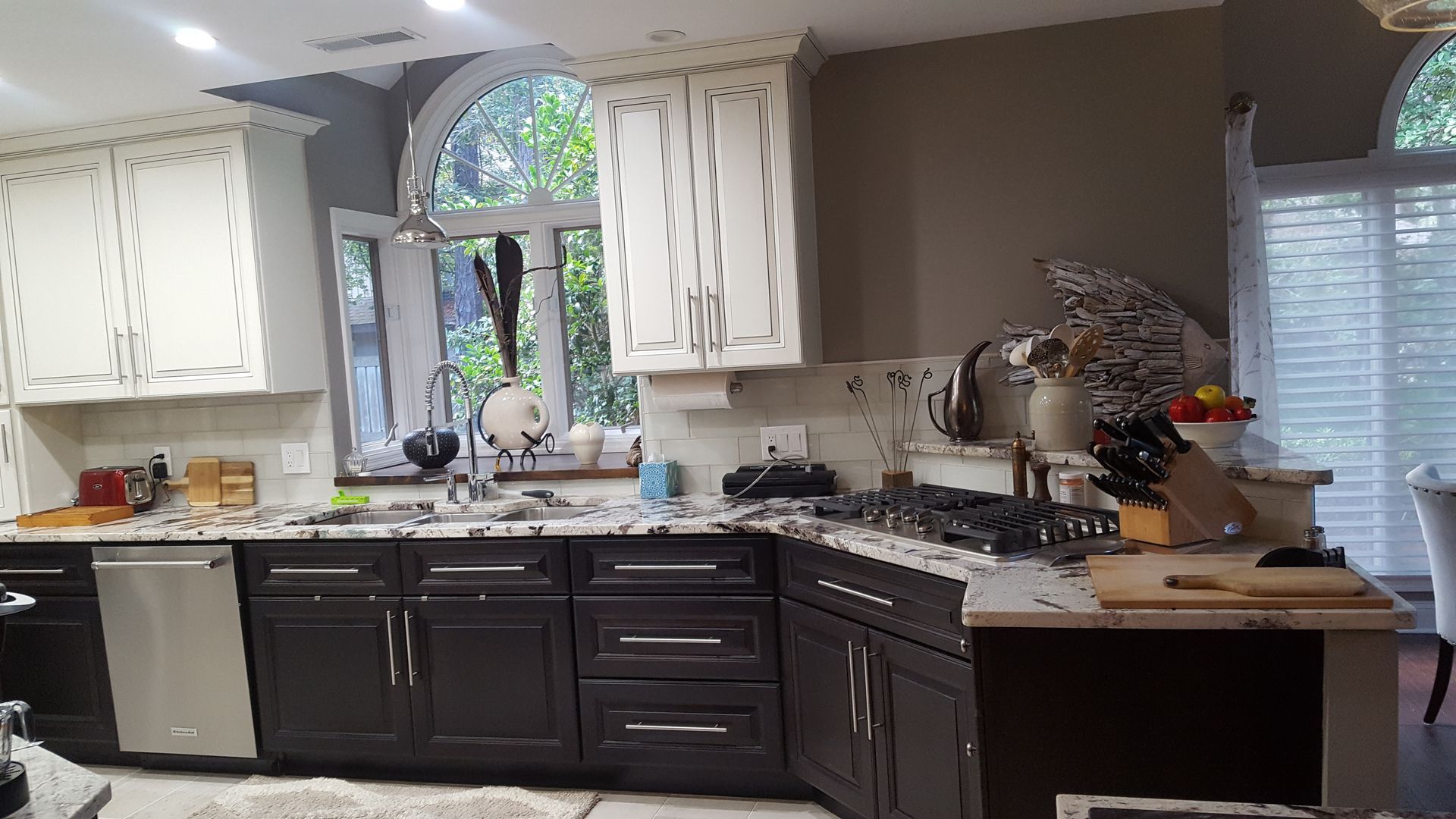 Kitchen with dark and light cabinets, granite countertops, and a window with foliage outside.