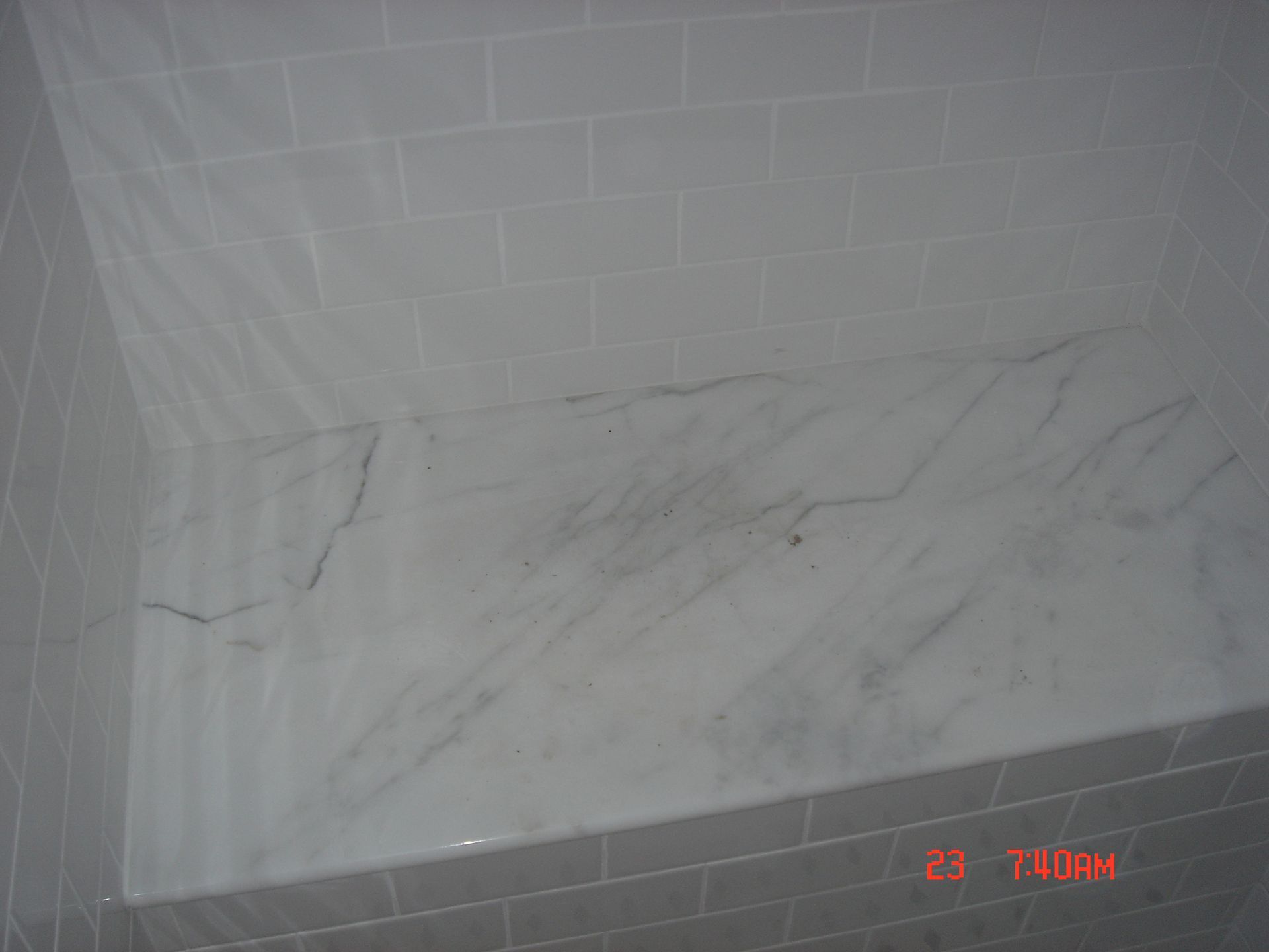 Shower interior with marble shelf and tiled walls, water damage visible.