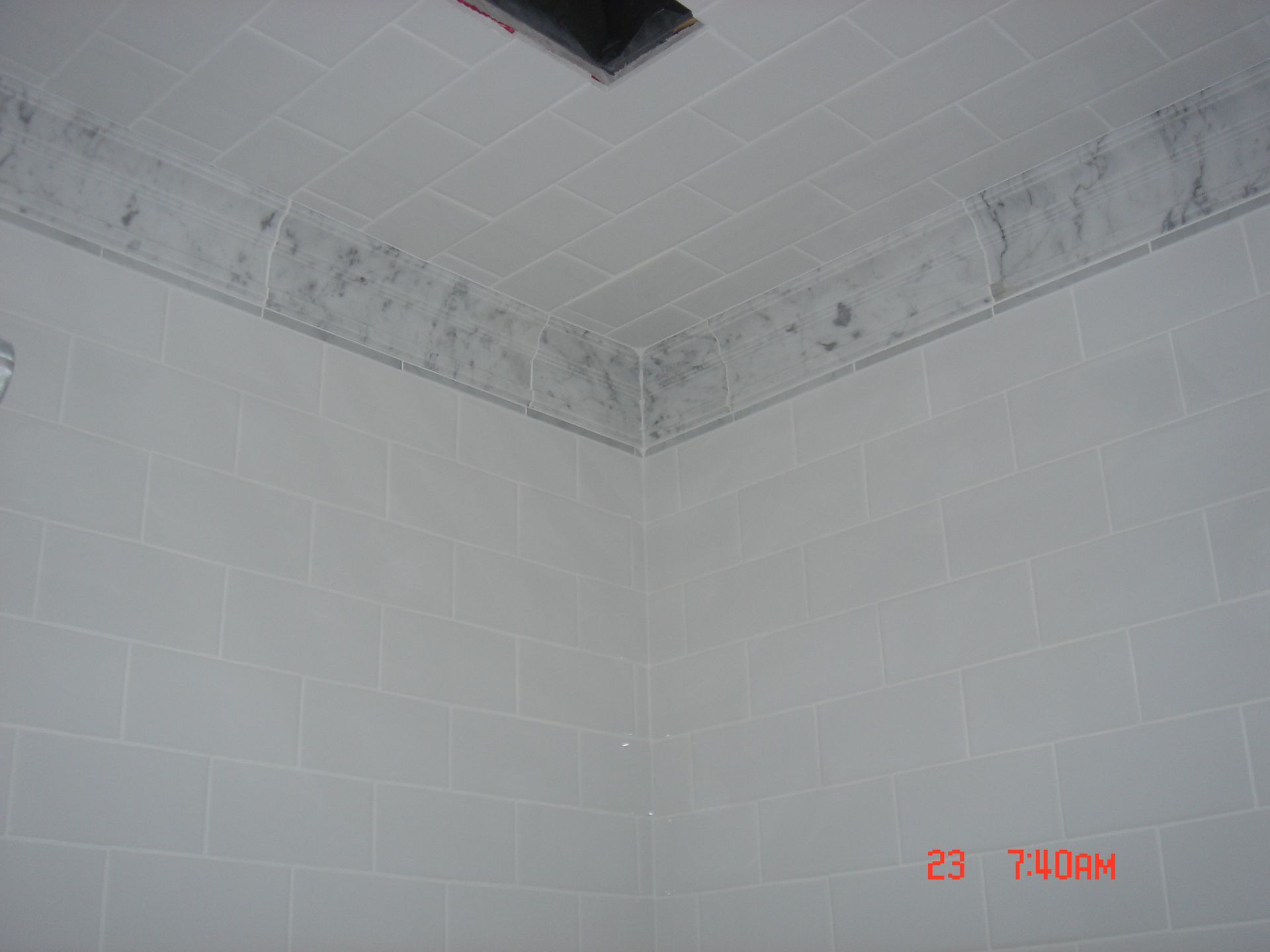 White tiled bathroom corner; dark mold growth on the tile trim near the ceiling.