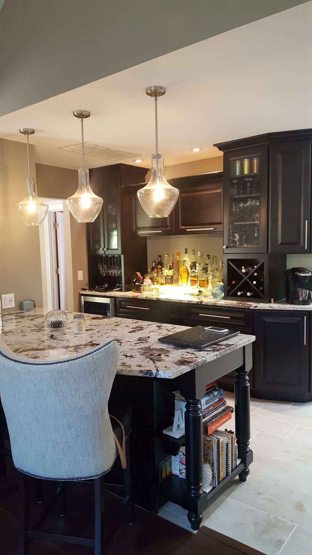 A kitchen with a black island, granite countertop, and pendant lights. A bar area is in the background.