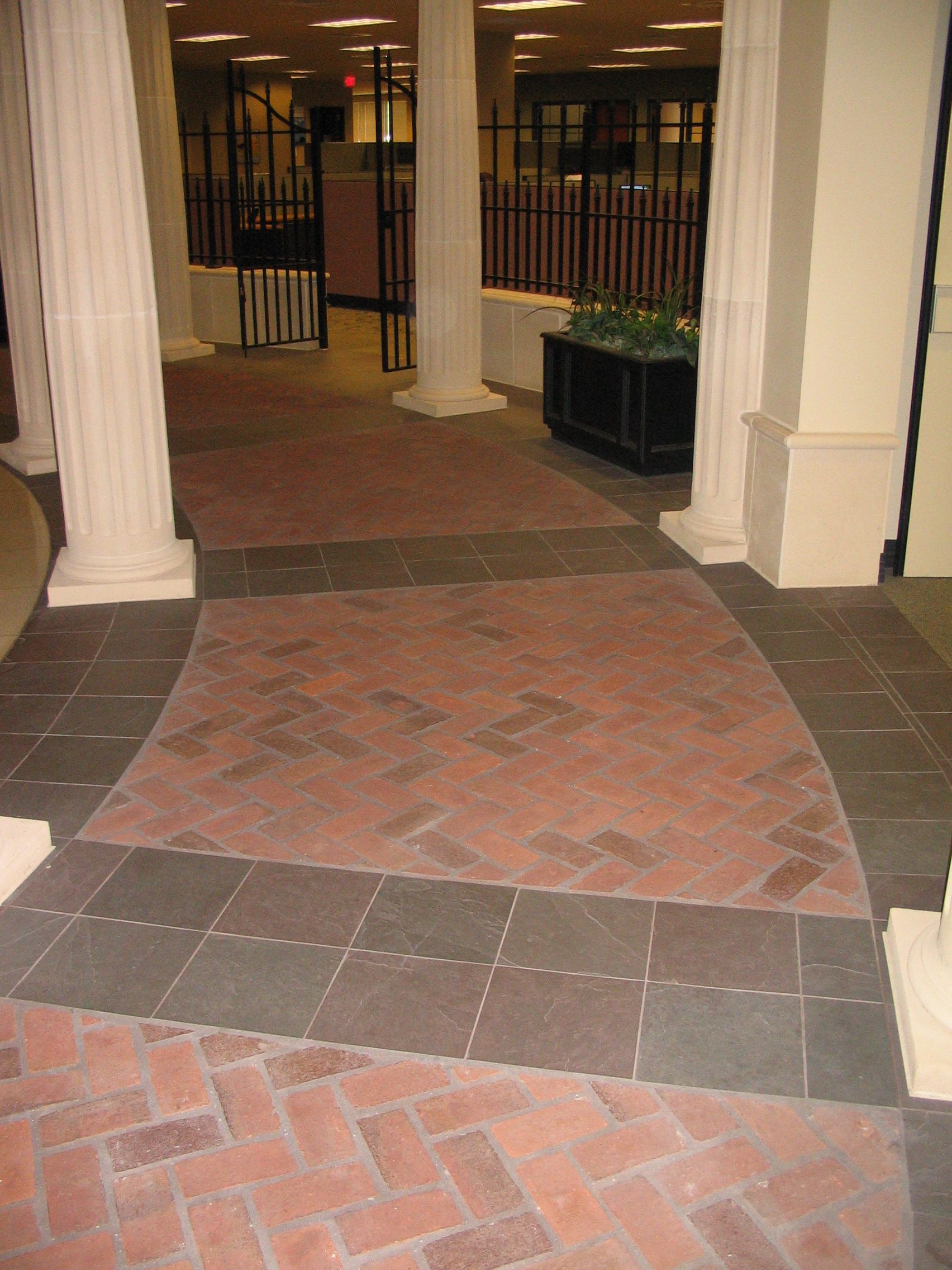 Hallway with brick and tile flooring, white pillars, and a distant doorway.