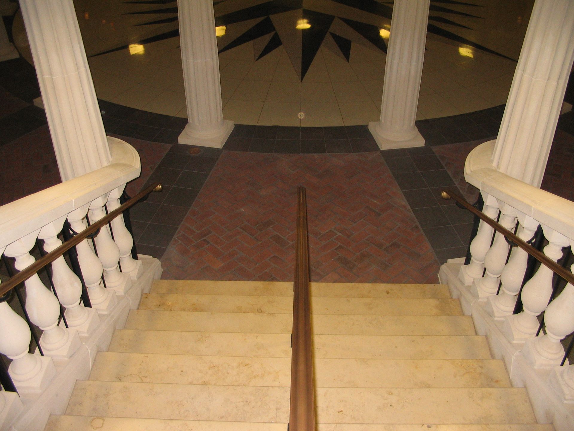 Staircase leading down from a hallway with pillars and decorative floor tiling.