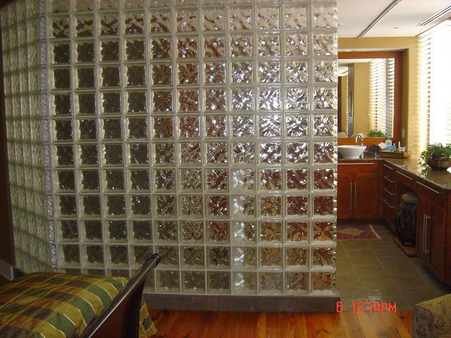 Glass block wall separates a bedroom from a bathroom, with wood floors and brown cabinets visible.