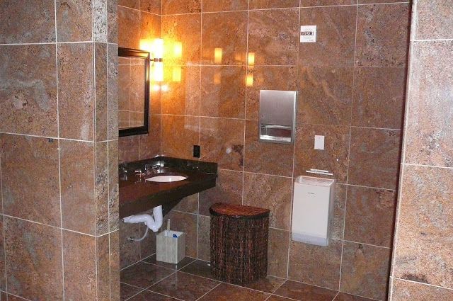 Bathroom with brown tile walls, sink, mirror, and a decorative trash can.