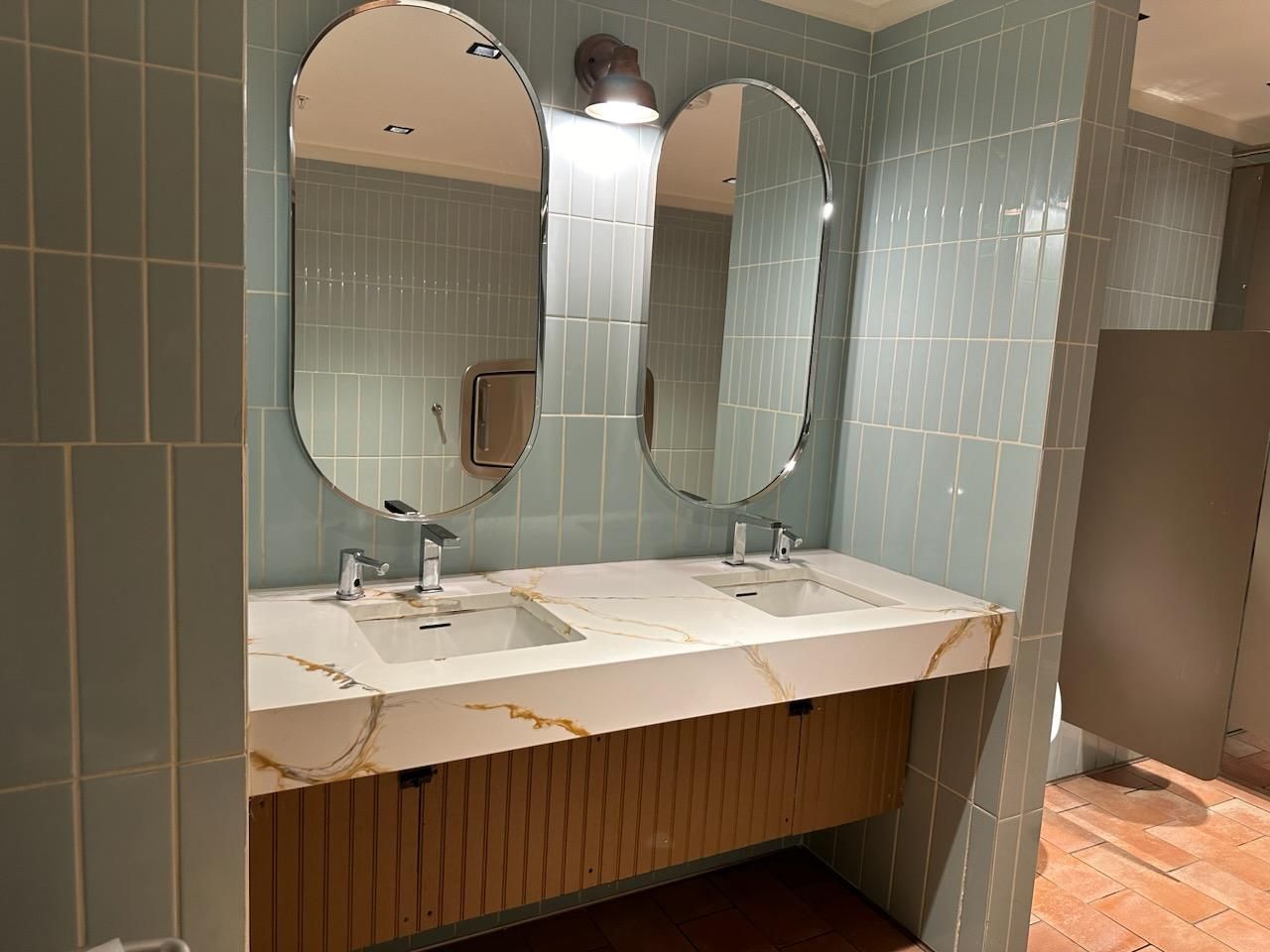 Public restroom with two sinks, oval mirrors, and light blue tile.