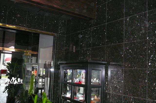 Black granite tiled wall with a glass display cabinet, reflecting a doorway and plants.