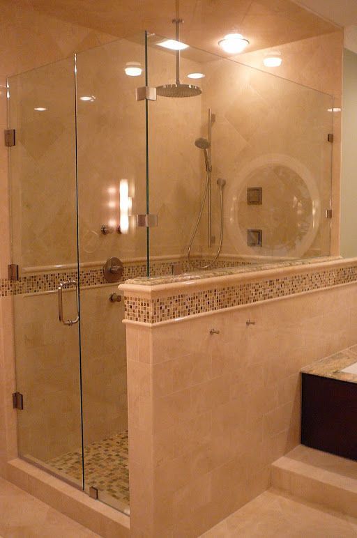 Luxurious beige tiled shower with glass doors, pebble floor, and rain showerhead.