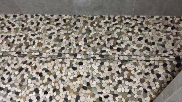 Close-up of a floor with pebble-like tiles in shades of green, brown, and white, with a linear drain.