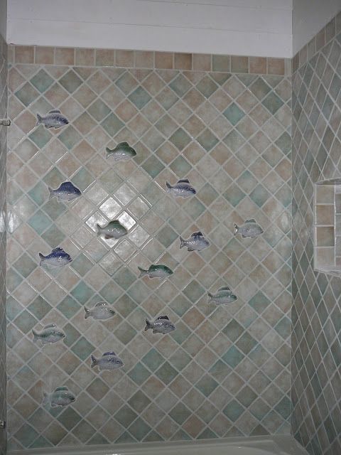 Shower wall with diamond pattern tiles and decorative fish. Turquoise and beige tones.