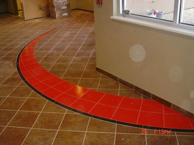Brown tiled floor with a red curved accent, black border, next to a beige wall with a window.